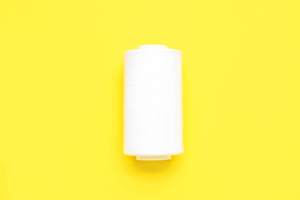 White thread spool on yellow background - Фото, изображение