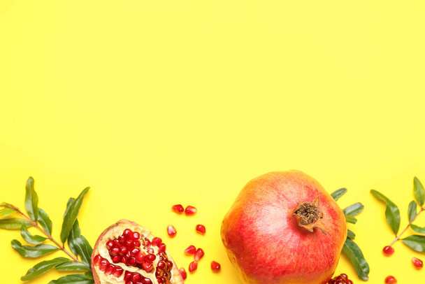 Composition with fresh pomegranates and plant branches on yellow background - Photo, Image