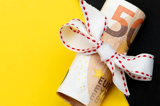 Rotolo di 50 Euro con nastro bianco isolato su sfondo giallo e nero, idea regalo denaro - Foto, immagini