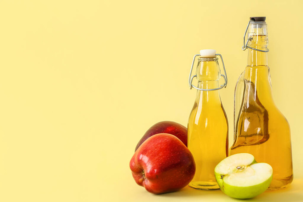 Bottles of apple cider vinegar and fruits on yellow background - Фото, зображення