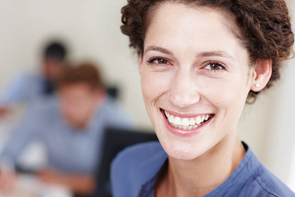 Positive corporate attitude. Closeup portrait of a smiling young businesswoman with her colleagues sitting in the background - Foto, imagen