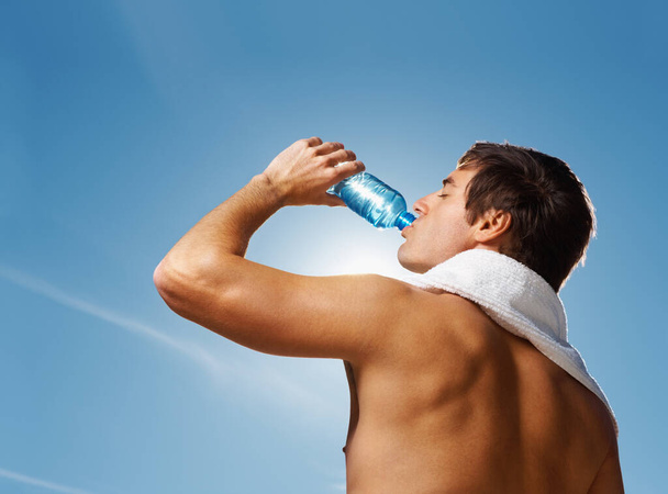 Young masculine man drinking water after a workout. Portrait of a shirtless man drinking water after his workout against the clear sky - Fotografie, Obrázek