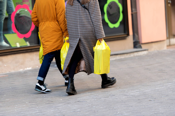 Rear view of two women carrying yellow plastic shopping bags - Valokuva, kuva