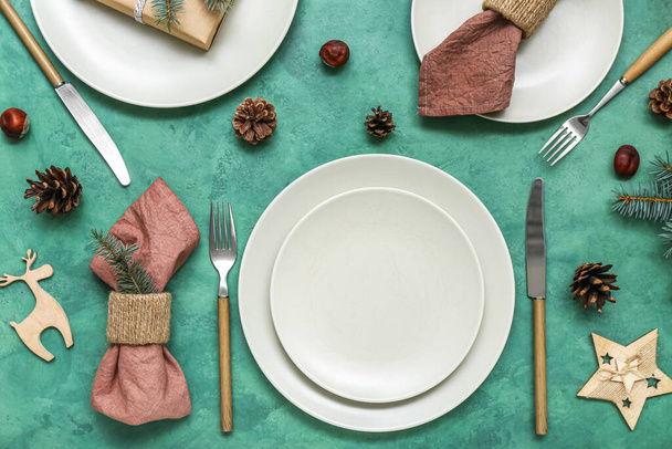 Beautiful table setting with Christmas decor and fir cones on green background - Photo, Image