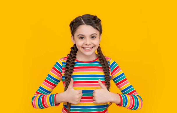 teen braided girl in childhood isolated on yellow background, thumb up. childhood of teen girl with braided hair in studio. photo of teen girl. childhood studio shot of teen girl. concept of childhood - Foto, Imagem