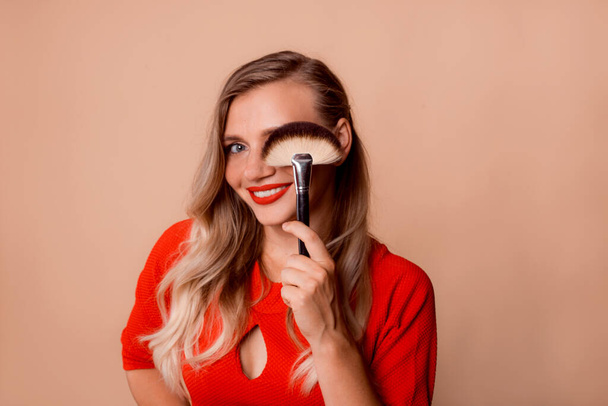 banner Fan borstel make-up accessoire voor losse texturen in vrouw hand in de buurt van gezicht op beige achtergrond - Foto, afbeelding