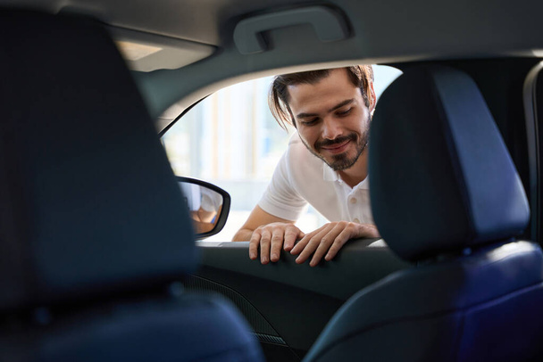 Smiling young automotive dealership customer looking inside passenger car through open window - Foto, Imagem
