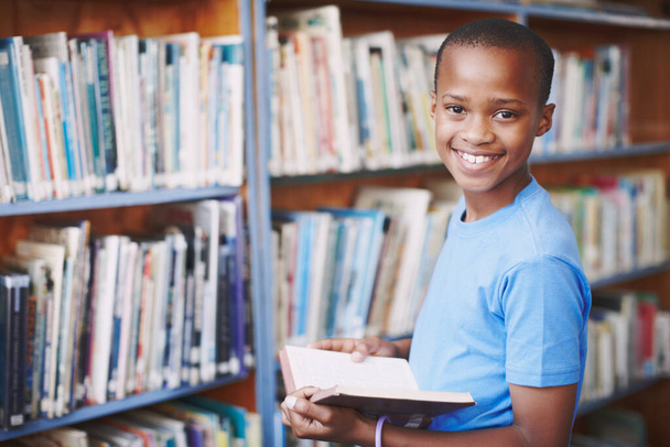 Stories are like new playgrounds. Portrait of an african american boy enjoying a good book at the library - 写真・画像