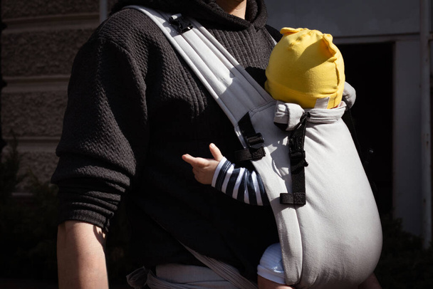 κοντινό πλάνο του πατέρα που κυοφορεί το παιδί του σε μια σφεντόνα μωρού - Φωτογραφία, εικόνα