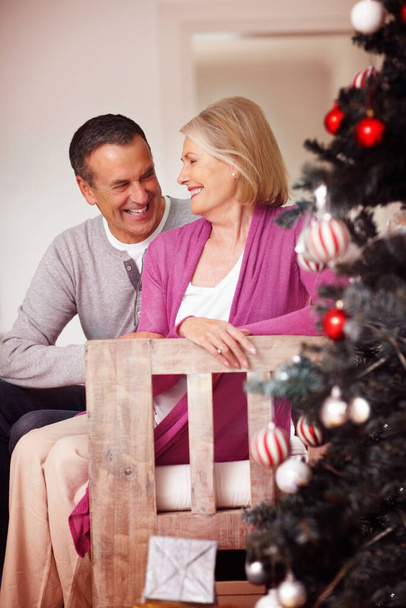 Loving mature couple near a Christmas tree looking at each other. Portrait of a loving mature couple near a Christmas tree looking at each other - 写真・画像