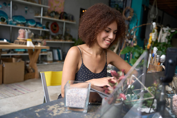 Joyous brunette lady smiling while working on laptop at her stylish florist workshop - Photo, Image