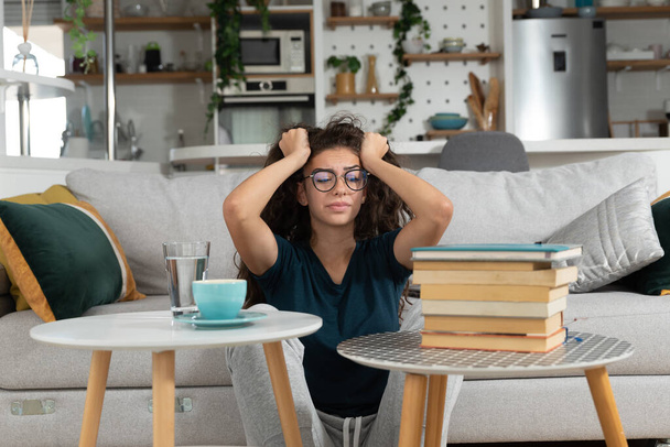 Young schoolgirl or university student has a headache when she sees how much she has to study in order to prepare for the exam and achieve knowledge after illness and absence from classes and lectures - Фото, изображение