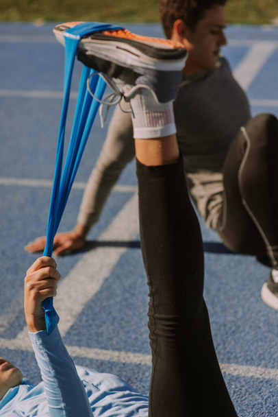 Een meisje traint haar beenpols terwijl haar mannelijke vriend zijn benen uitstrekt. - Foto, afbeelding