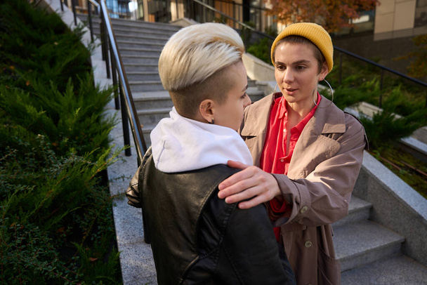 Two young women communicate on the city steps, the brunette put her hands on the shoulders of the blonde - Photo, Image
