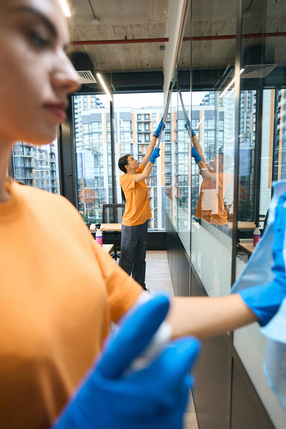 Employees of cleaning company in overalls treat glass partitions in coworking space with a disinfectant, they work in rubber gloves - Fotoğraf, Görsel