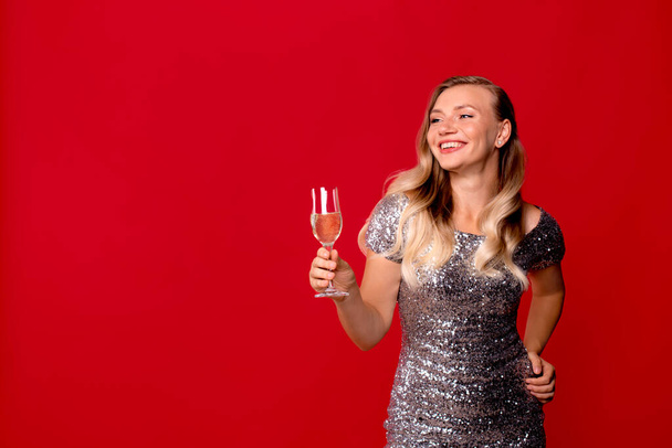 krásná mladá dívka se sklenkou šampaňského na červeném pozadí studia. - Fotografie, Obrázek