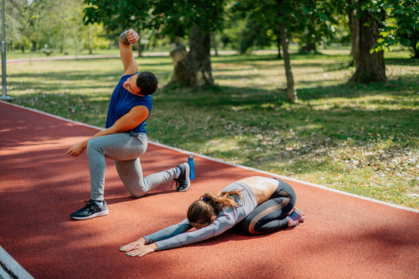 Un hombre guapo y una hermosa mujer deportista están haciendo ejercicio juntos en el parque, en un día soleado - Foto, Imagen