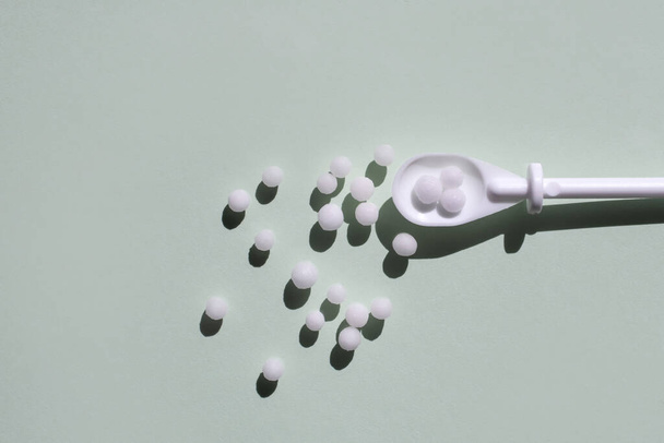 Die homöopathischen Pillen sind auf hellgrünem Hintergrund verstreut. Flaches Styling, Raum für Text. Konzept der alternativen Medizin. - Foto, Bild