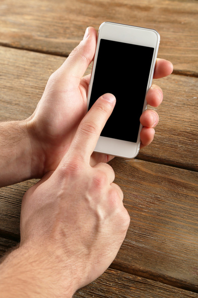 Hands holding smart mobile phone on wooden table background - 写真・画像