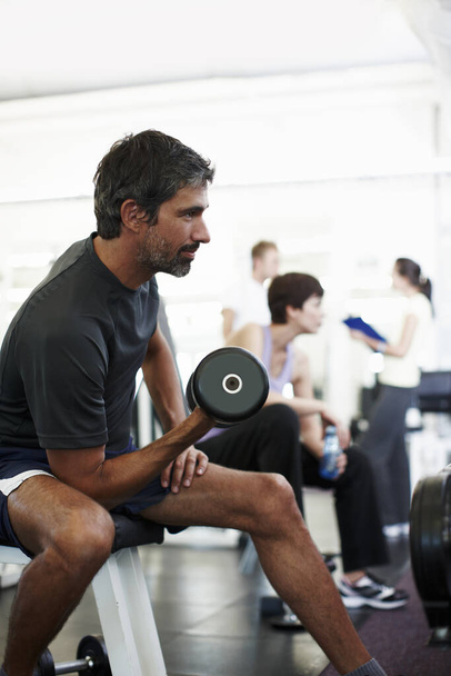Keeping fit. a handsome man working out with weights in the gym - 写真・画像