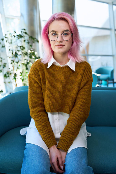 Pretty woman with pink hair sitting on the sofa in office and looking at the camera - Fotoğraf, Görsel
