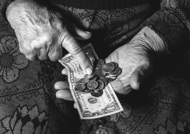 Старуха с очень малыми деньгами. Концепция бедности. Пенсионер с долларовой банкнотой и монетами в руках. Экономика и кризис в мире. - Фото, изображение
