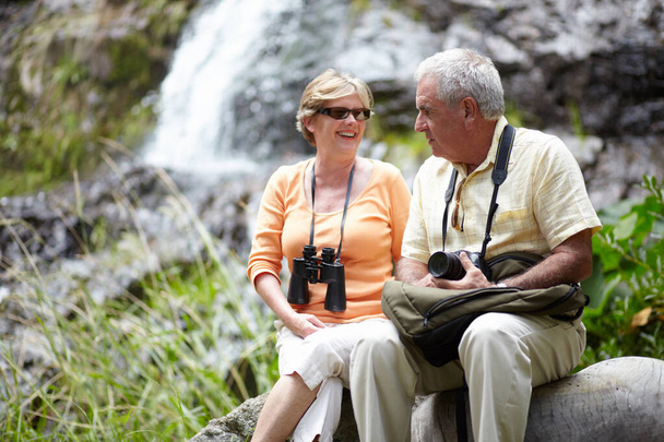 This place is beautiful. A loving senior couple stopping for a break by a waterfall while out for a walk in nature - 写真・画像