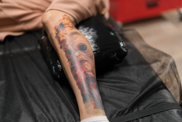Tatuaje con un extraterrestre en la pierna de una mujer durante una sesión de corrección de tatuaje en un estudio de tatuaje - Foto, Imagen
