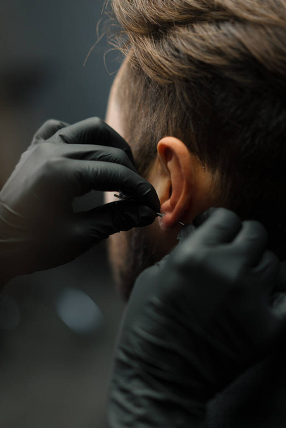 Tattoo piercing studio - woman makes an ear piercing to a man to a guy - Photo, image