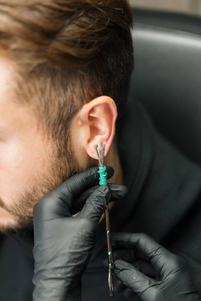 Tatuaggio piercing studio - donna fa un orecchio piercing a un uomo a un ragazzo - Foto, immagini