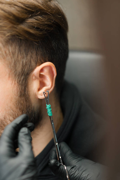 Tatuagem piercing estúdio - mulher faz uma orelha piercing para um homem para um cara - Foto, Imagem