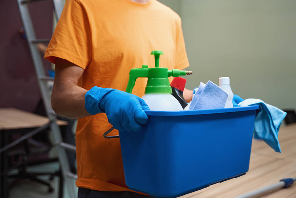 Cropped photo of man in rubber gloves holding a box full of housecleaning equipment - Foto, imagen