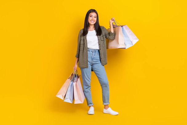 Full body size foto van jonge lachende positieve japanse dame dragen casual outfit houden boodschappentassen nieuw merk aanbod geïsoleerd op gele kleur achtergrond. - Foto, afbeelding