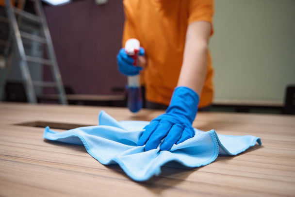 Обрезанный кадр очистителя в резиновых перчатках с использованием дезинфицирующего спрея и ткани для очистки поверхности - Фото, изображение