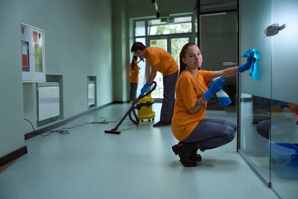 Junges Team professioneller Reinigungskräfte räumt auf und staubsaugt Flur im Gebäude - Foto, Bild