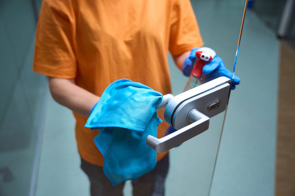 Zugeschnittenes Foto eines Servicemitarbeiters in Uniform, der sich um die Sauberkeit der Glastüren kümmert - Foto, Bild