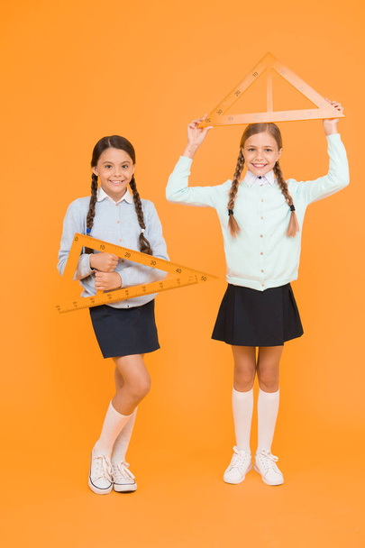 Measuring angles at geometry. Cute schoolgirls holding triangles for geometry lesson on yellow background. Little girls learning geometry. Small children with geometrical tools for geometry. - Фото, изображение
