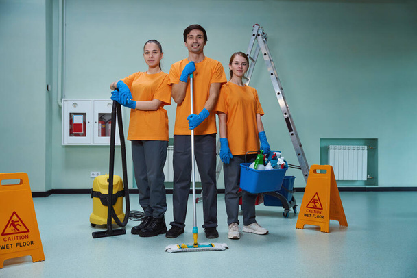 Велика команда професійних прибиральників тримає різні види побутового обладнання і посміхається в камері
 - Фото, зображення