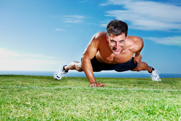 Young guy doing single handed pushups on the field. Portrait of a young guy doing single handed pushups on the grass field - Copyspace - Valokuva, kuva