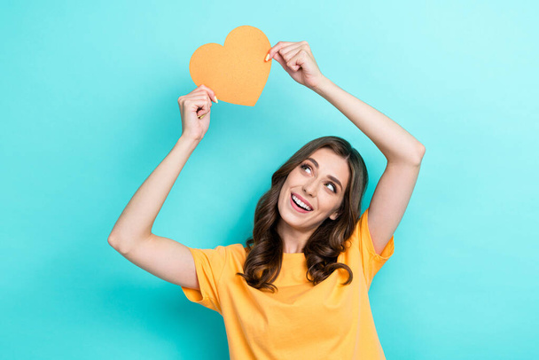 Photo of dreamy shiny lady wear yellow t-shirt rising orange heart looking empty space isolated turquoise color background. - 写真・画像