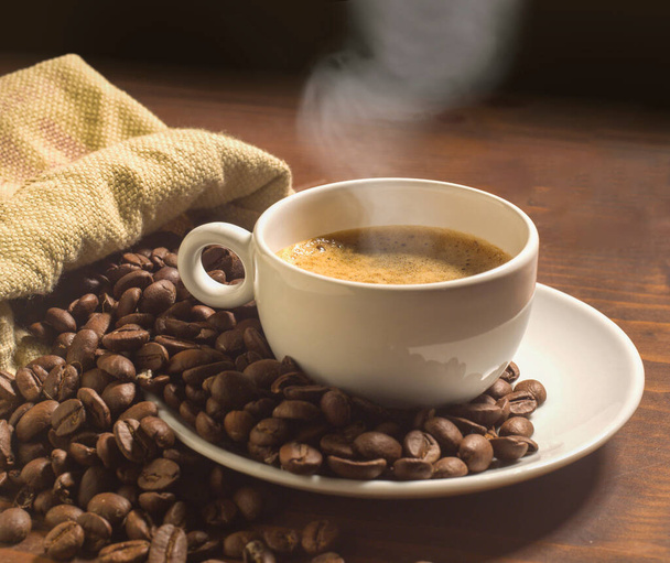 tasse de café avec soucoupe et grains de café tout autour sur la table en bois - Photo, image