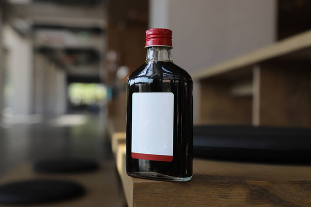 Isolierte kalte Brühkaffeeflasche oder Getränkeflasche. Fotografiert in natürlichem Licht, Holzböden und schönem Raum. Leerer Raum für Botschaft oder Marke - Foto, Bild