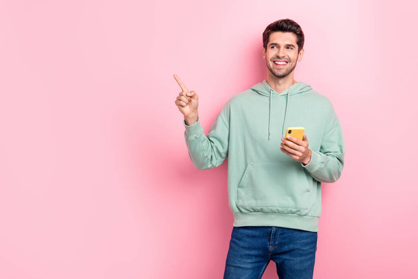 Photo of young positive excited interested businessman wear green sweatshirt finger pointing look empty space promo app phone isolated on pink color background. - Valokuva, kuva