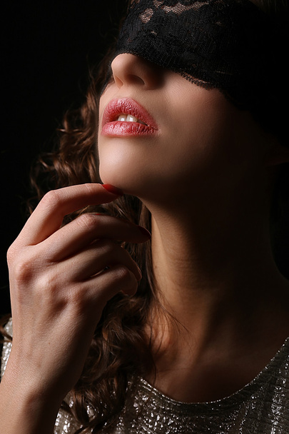Beautiful girl in lace mask over eyes on dark background - Fotó, kép