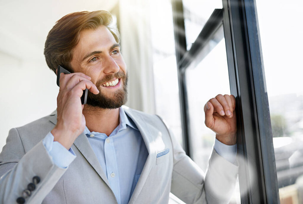 Рад, что вы решили инвестировать с нами. молодой бизнесмен разговаривает по мобильному телефону, стоя у окна своего офиса - Фото, изображение
