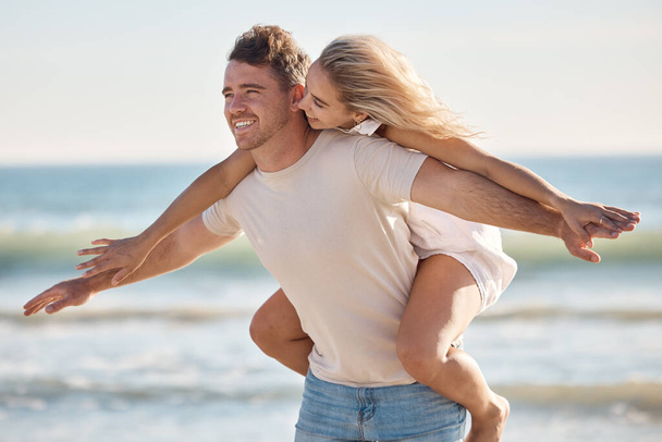 Couple, freedom and love at the beach, together and piggyback on adventure with travel and ocean. Trust, relationship and man with happy woman, seaside vacation with arms out and care free - Foto, imagen