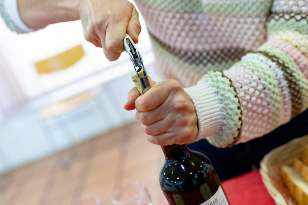 Tirbuşon. Geldi. Tirbuşonla kırmızı şarap şişesini açma zamanı. Mantarı açarken kadının elleri şişeyi tutuyor. Yatay fotoğrafçılık. - Fotoğraf, Görsel