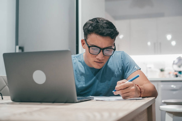 Yksi nuori teini opiskelee ja työskentelee kotona yöllä pöydällä kannettavan tietokoneen hymyillen ja pitämällä hauskaa läksyjen tekemisessä. - Valokuva, kuva