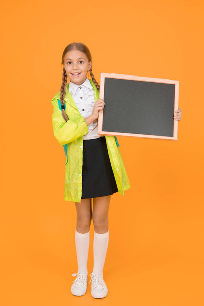 Placement of ad. Little child hold blank blackboard for information on yellow background. Small schoolgirl smile with tidy information board. Sharing happy information. Your information, copy space. - Foto, imagen