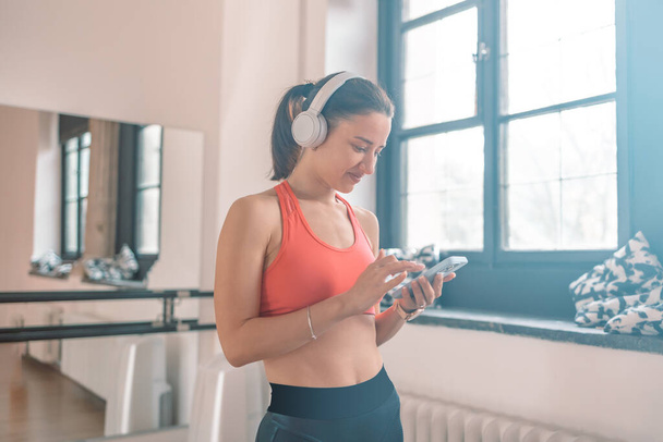 Активна молода кавказька спортивна інструкторка з фітнесу жінка використовує смартфон, слухаючи музику в тренажерному залі. Концепція тренувального спорту
.  - Фото, зображення